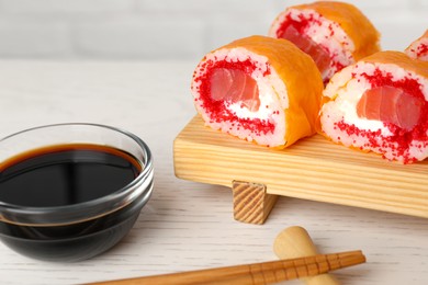 Photo of Delicious sushi rolls with salmon, chopsticks and soy sauce on white wooden table, closeup