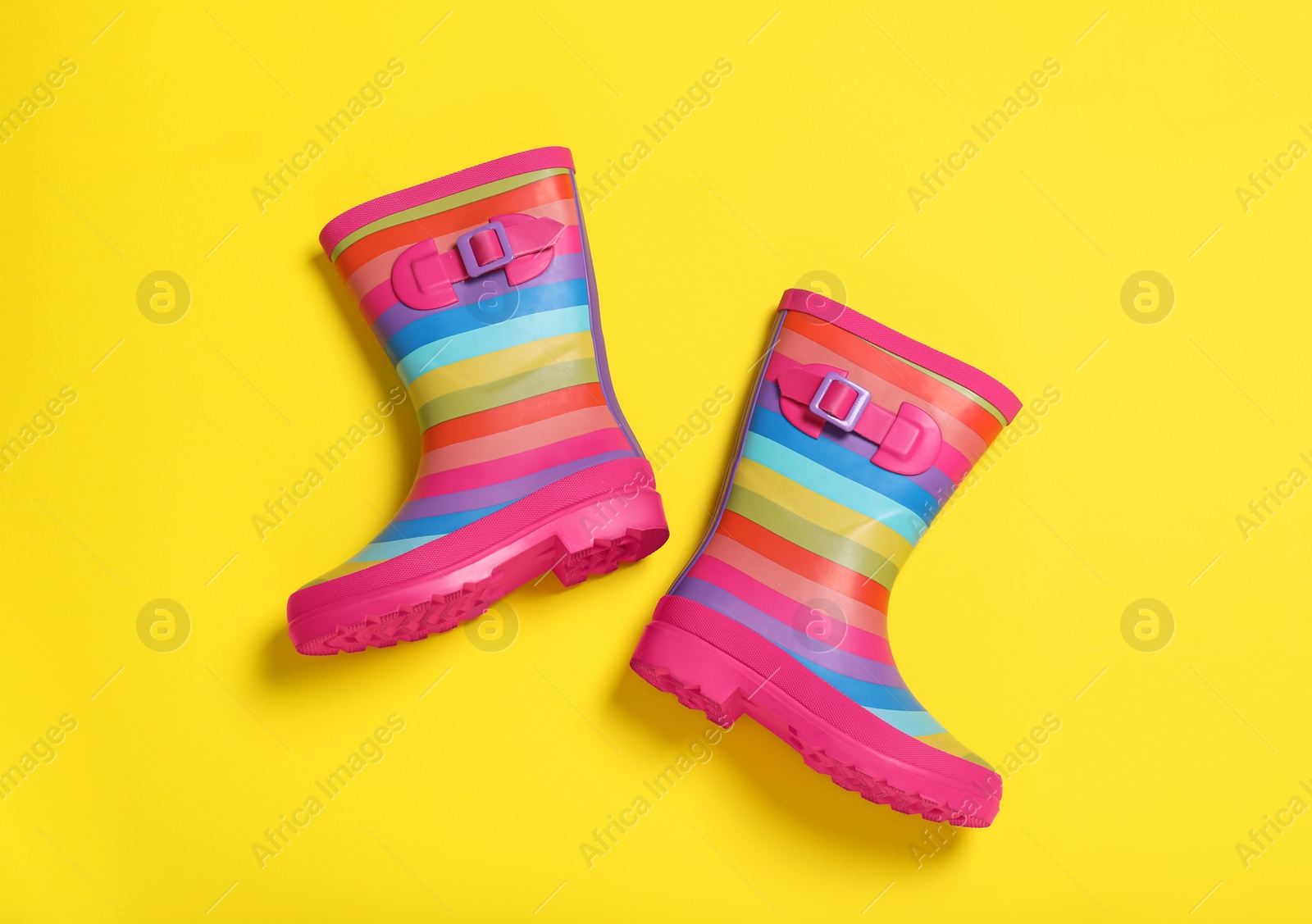 Photo of Pair of striped rubber boots on yellow background, top view