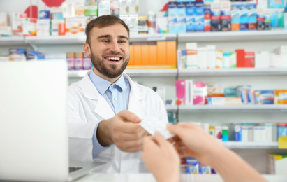 Image of Professional pharmacist giving pills to customer in modern drugstore