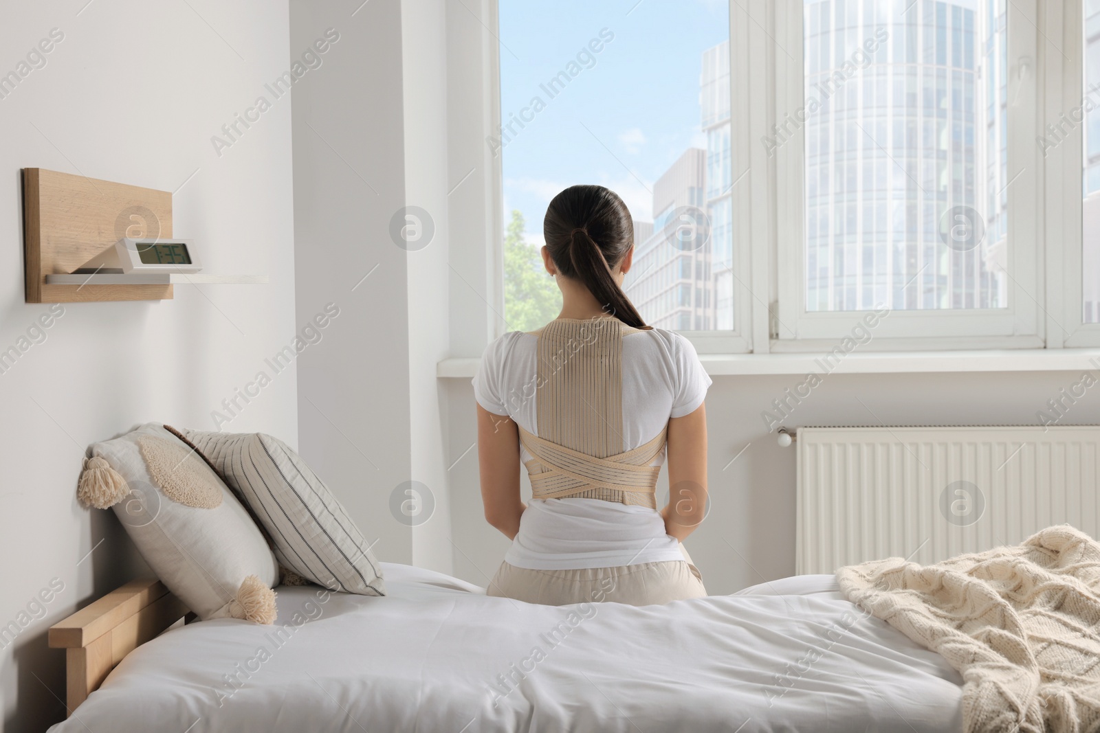 Photo of Woman with orthopedic corset sitting in bedroom, back view