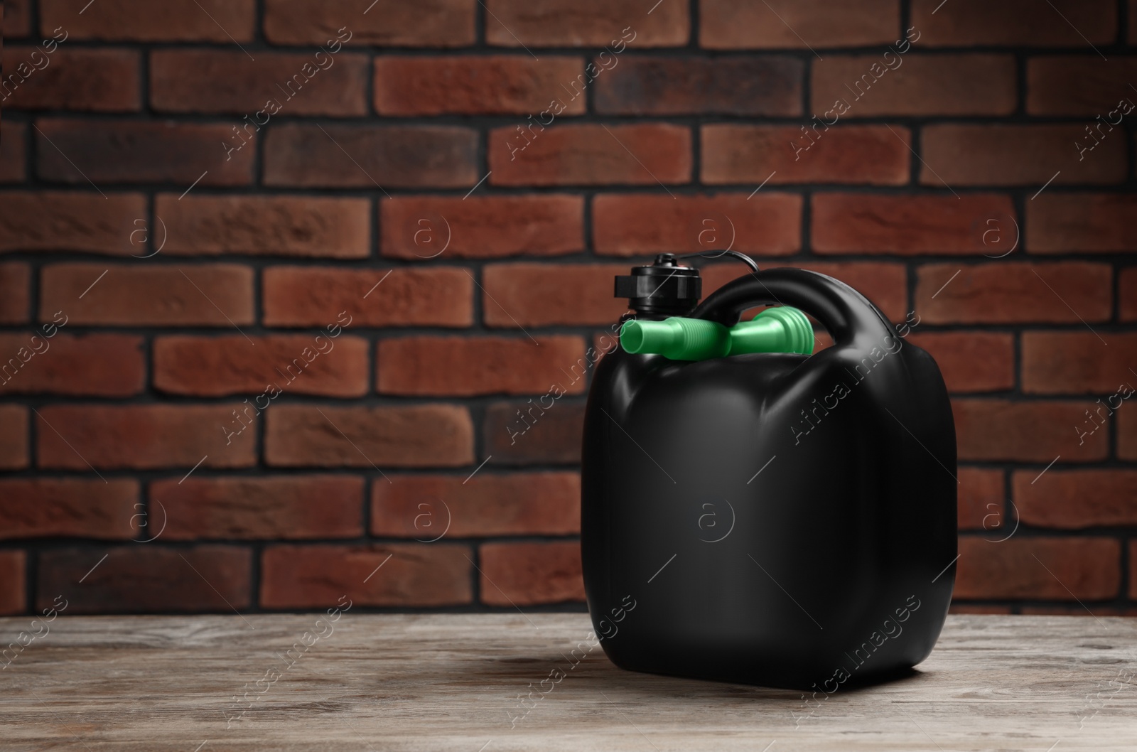 Photo of Black plastic canister on wooden table against brick wall, space for text