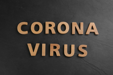 Photo of Words CORONA VIRUS made of wooden letters on black table, top view