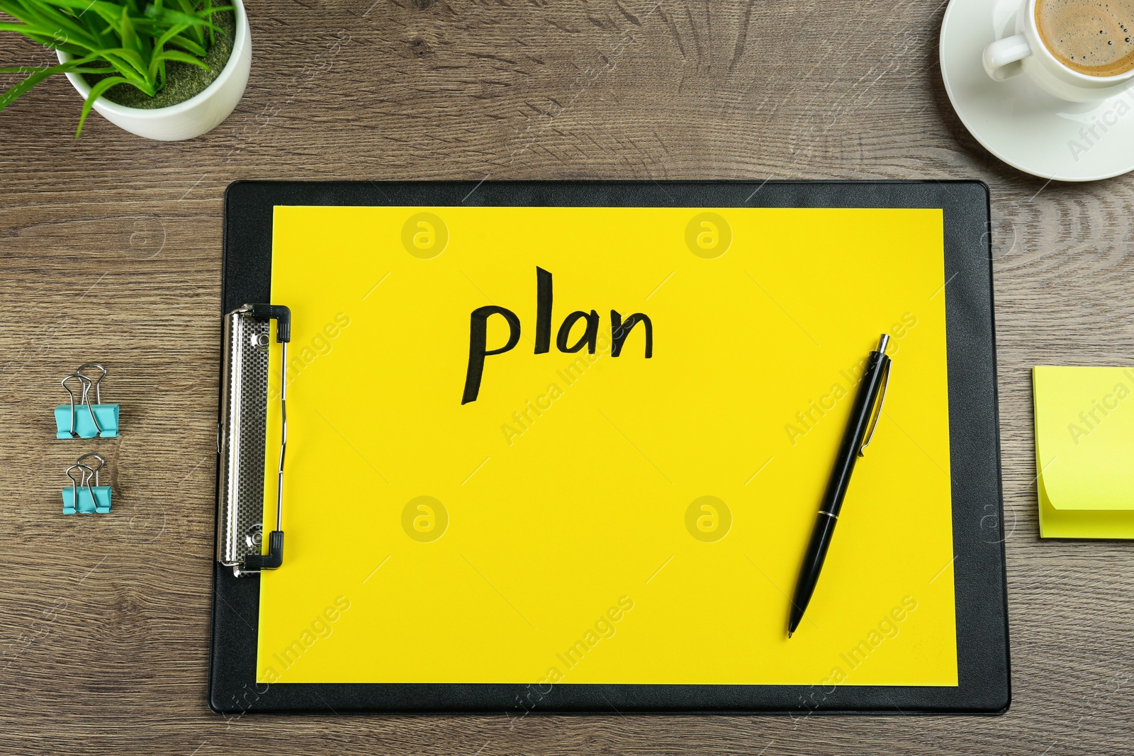 Photo of Paper with word Plan, pen, binder clips, coffee and houseplant on wooden table, flat lay