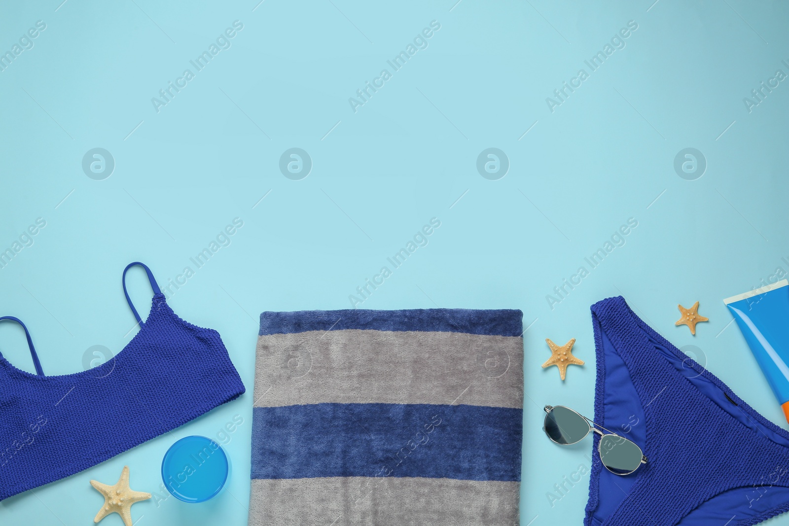 Photo of Beach towel, swimsuit, sunglasses sun and protection product on light blue background, flat lay. Space for text