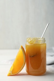 Delicious orange marmalade in jar on white table, space for text