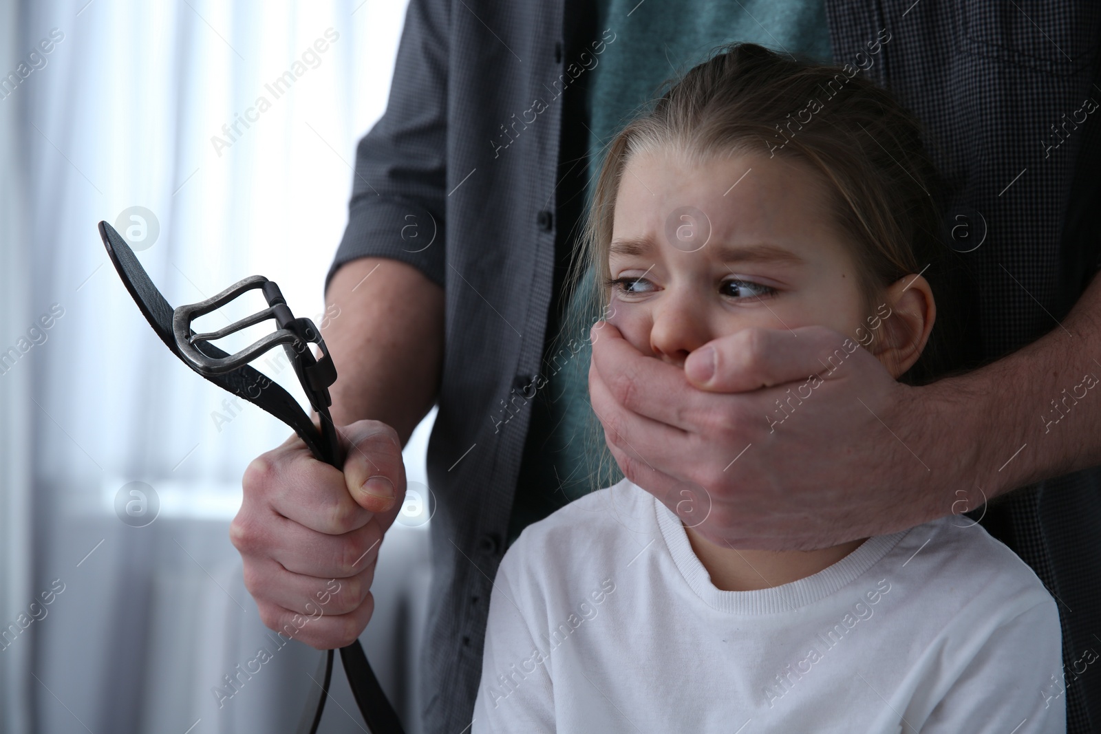 Photo of Man with belt covering scared little girl's mouth indoors. Domestic violence