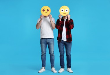 People covering faces with emoticons on light blue background