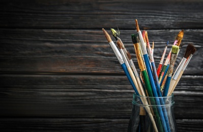 Jar with paint brushes on wooden background. Space for text