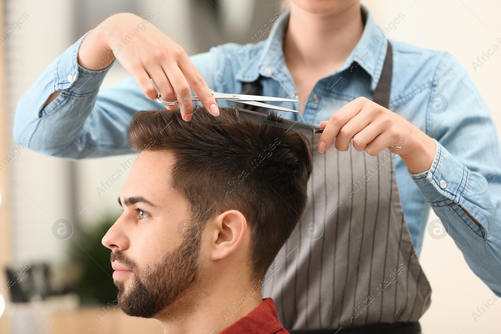 Photo of Barber making stylish haircut with professional scissors in beauty salon