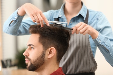 Photo of Barber making stylish haircut with professional scissors in beauty salon