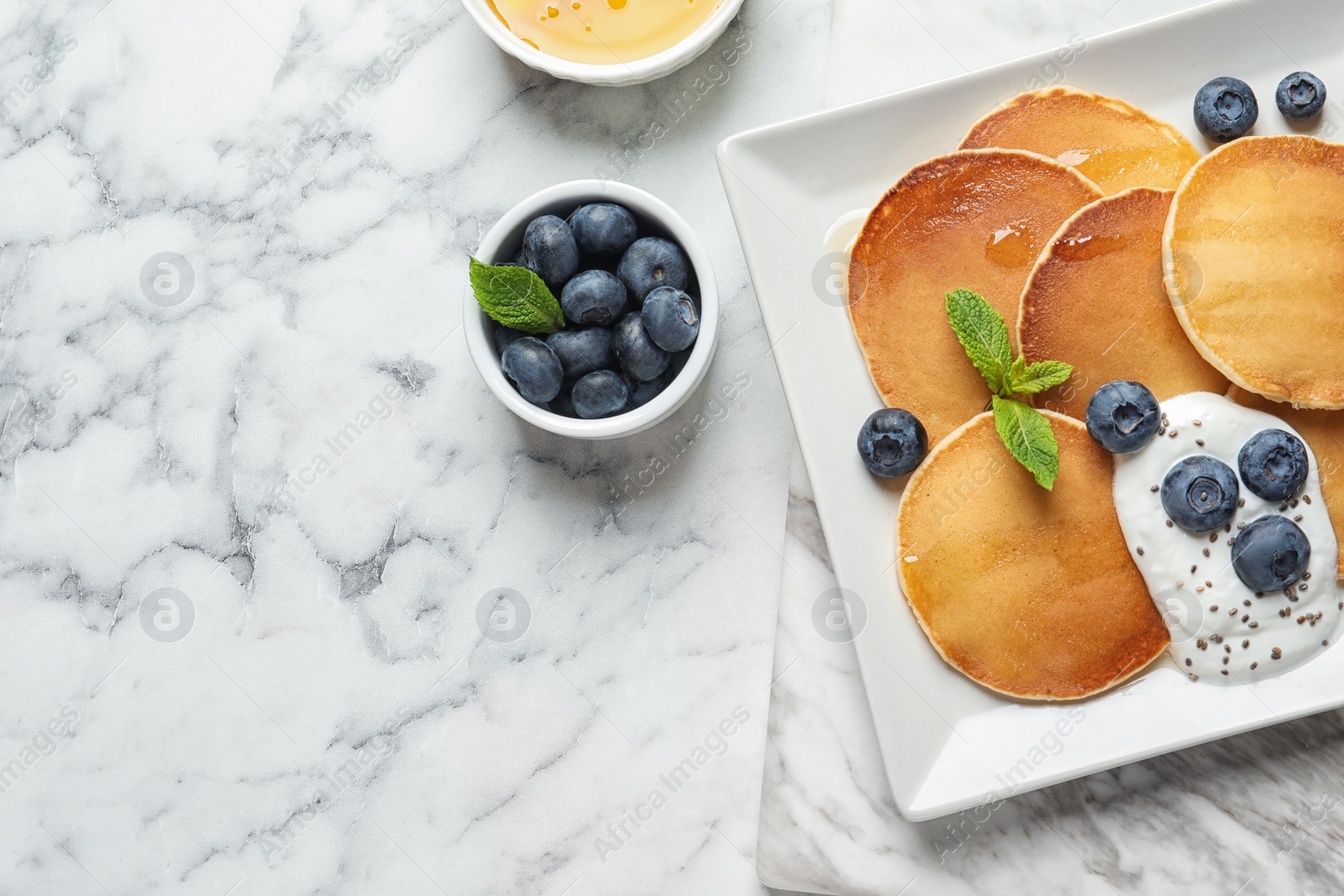 Photo of Plate of tasty pancakes with blueberries, sauce and mint on white marble table, flat lay. Space for text