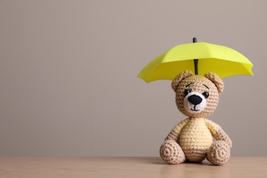 Photo of Small umbrella and toy bear on wooden table. Space for text