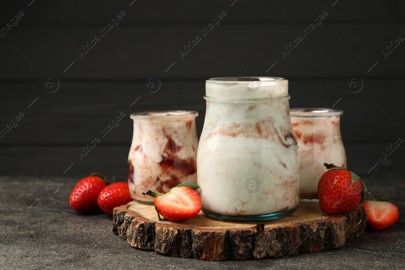 Photo of Tasty yoghurt with jam and strawberries on grey textured table, closeup