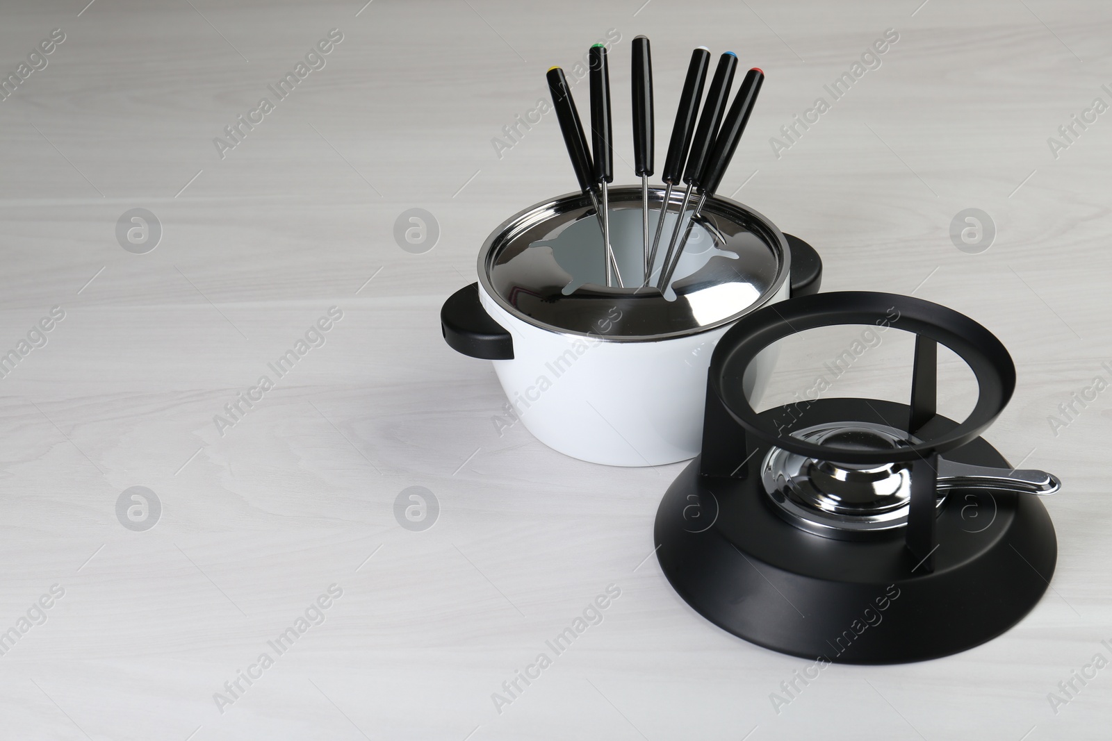 Photo of Fondue set on white wooden table, space for text