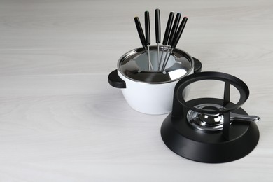 Fondue set on white wooden table, space for text