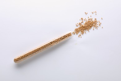 Photo of Glass tube with mustard seeds on white background, top view