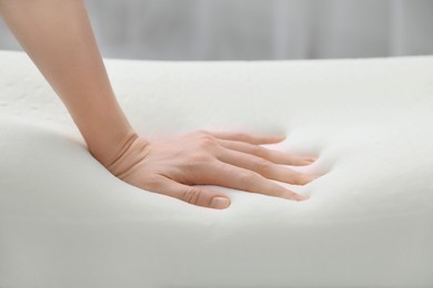 Woman touching orthopedic memory foam pillow indoors, closeup
