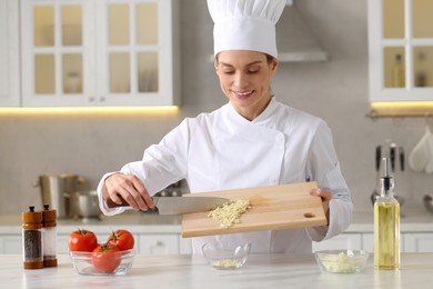 Professional chef putting cut garlic into bowl at white marble table indoors