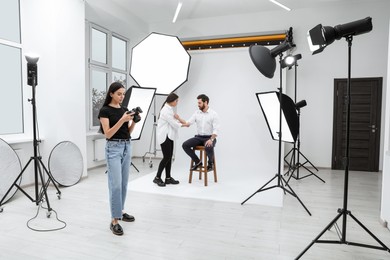 Professional photographer and stylist working with model in modern photo studio