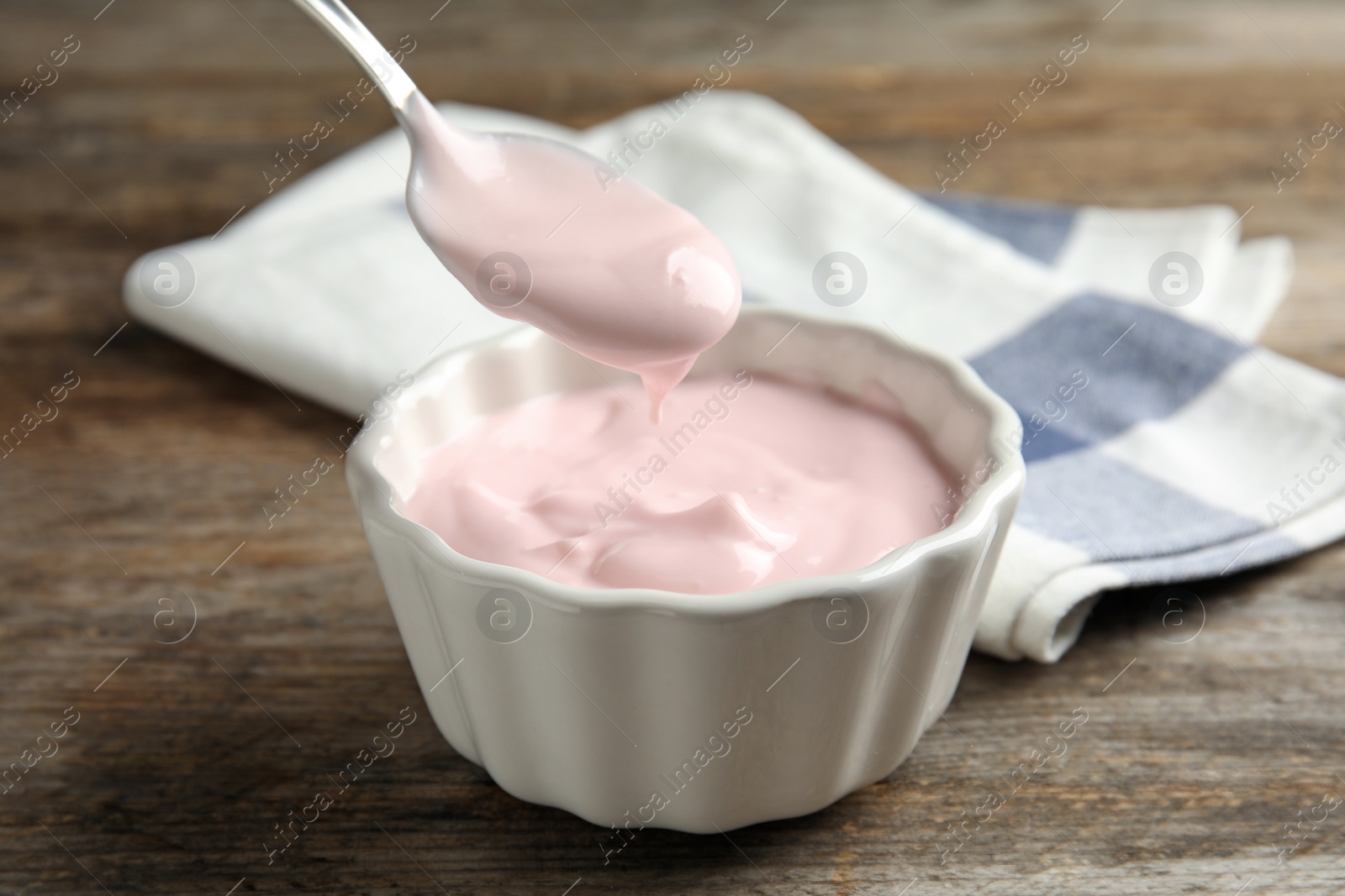 Photo of Spoon with creamy yogurt over bowl on wooden table