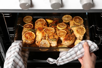 Photo of Woman taking delicious lemon chicken out of oven, closeup