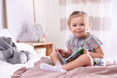 Cute little girl with book on bed at home