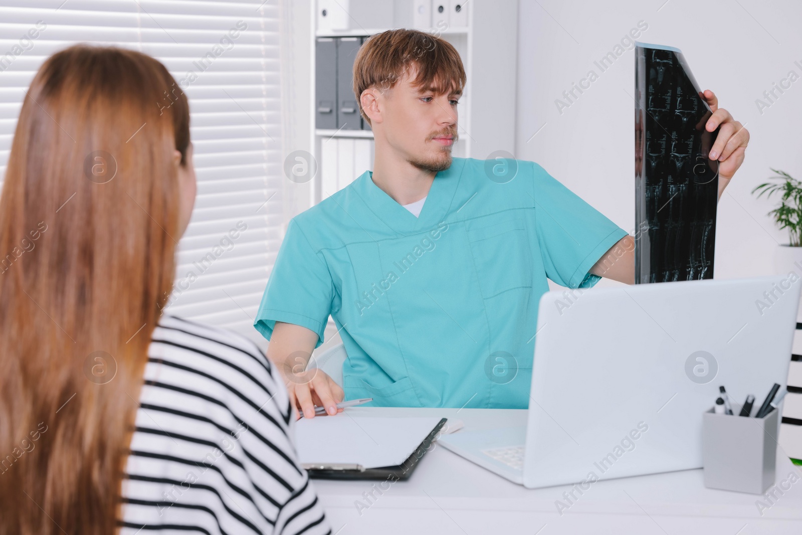 Photo of Doctor with neck MRI image consulting patient in clinic