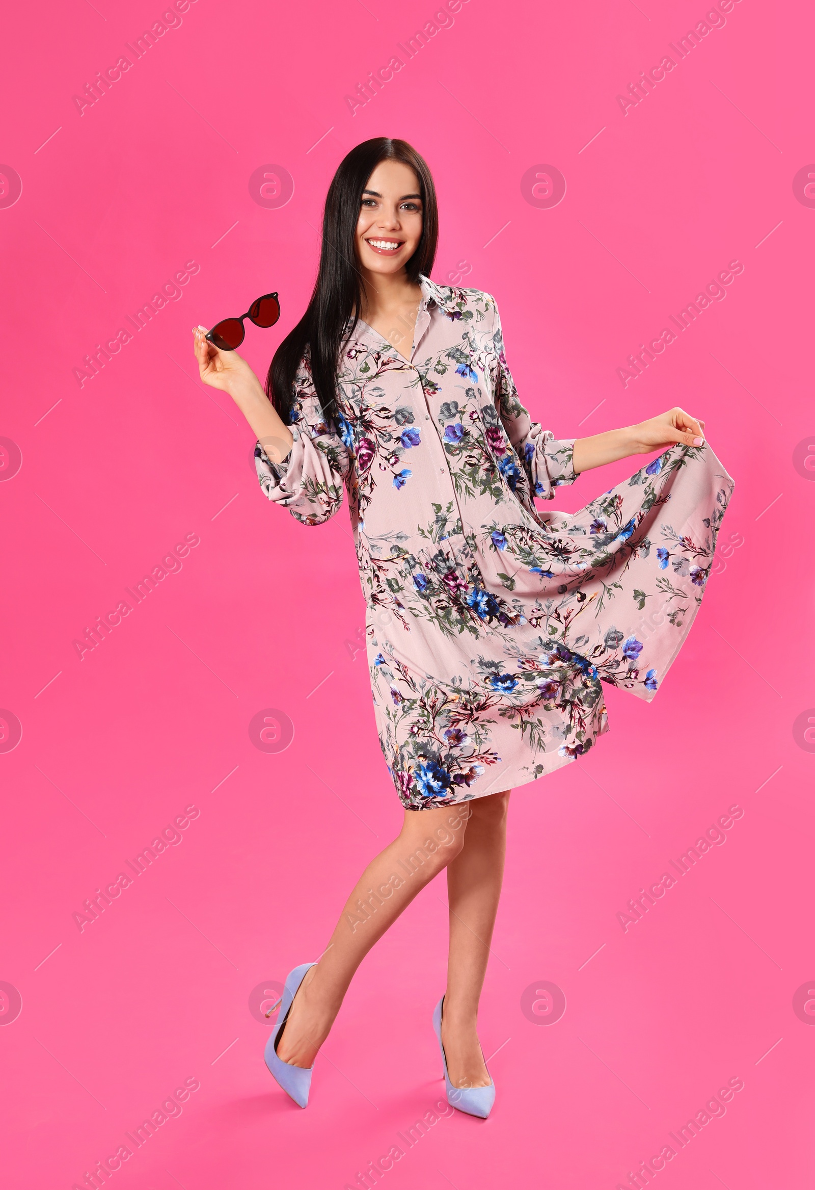 Photo of Young woman wearing floral print dress with stylish sunglasses on pink background