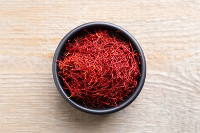 Photo of Dried saffron in bowl on wooden table, top view