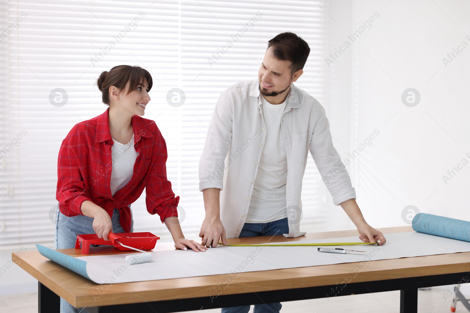 Photo of Woman and man applying glue onto wallpaper sheet at wooden table indoors