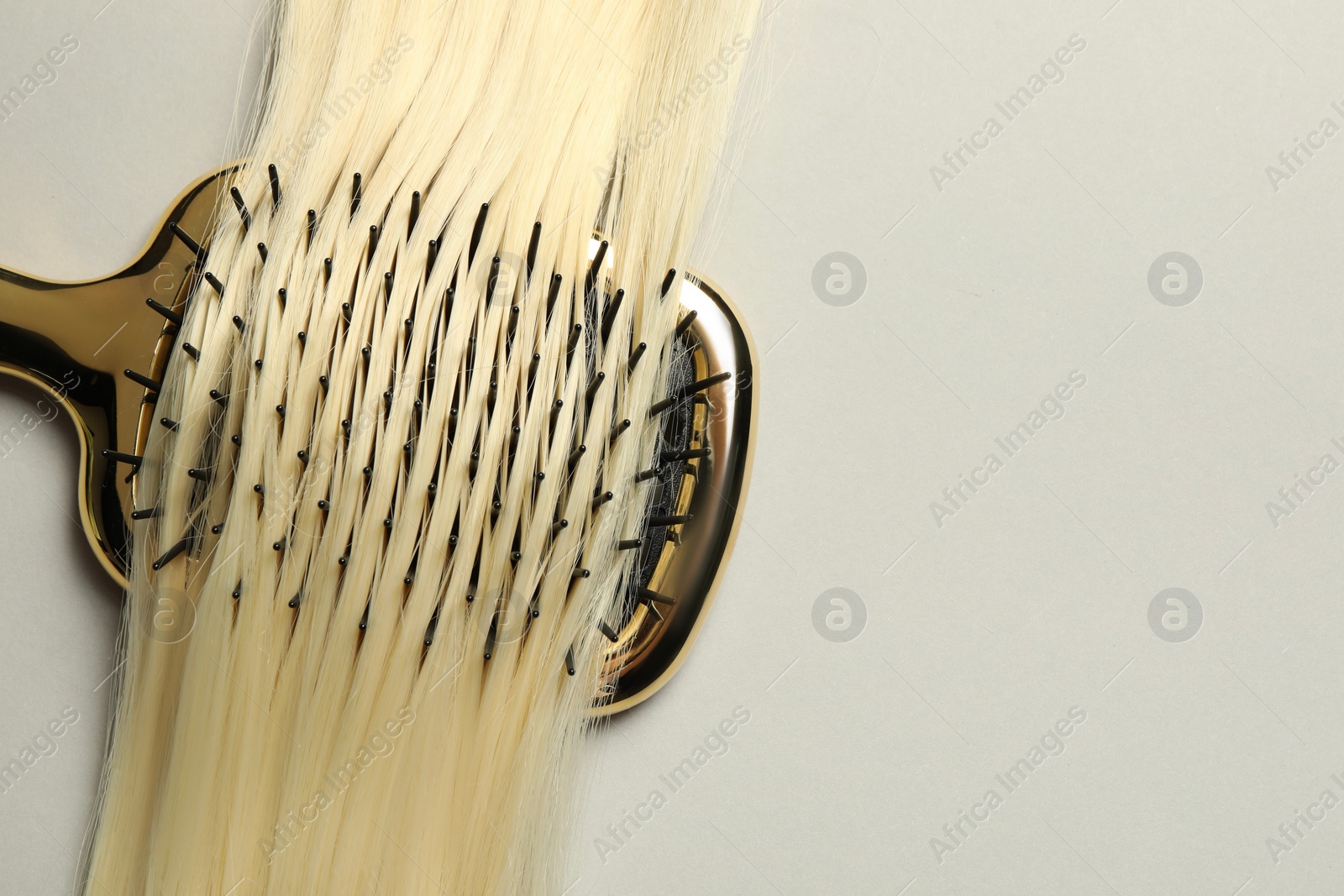 Photo of Stylish brush with blonde hair strand on light grey background, top view. Space for text