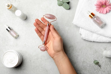 Photo of Woman with natural face roller at grey table, top view