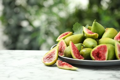Cut and whole green figs on white marble table against blurred background, space for text