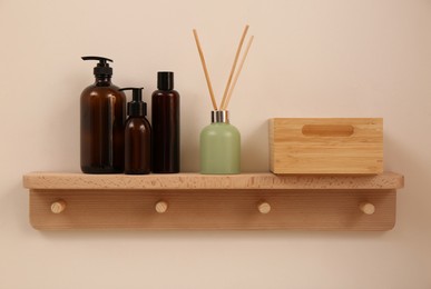 Wooden shelf with soap dispensers and aromatic reed freshener on beige wall. Interior element