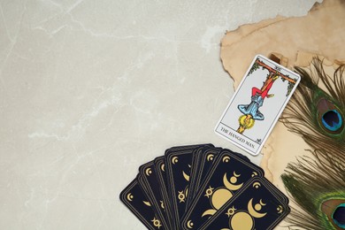 The Hanged Man and other tarot cards near peacock feathers on light table, flat lay. Space for text