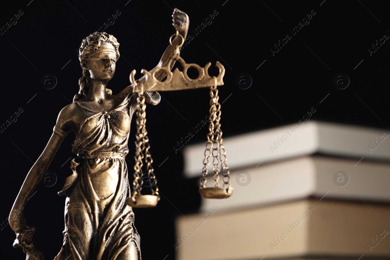Photo of Symbol of fair treatment under law. Statue of Lady Justice near books on dark background, closeup with space for text