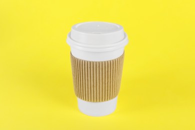 Paper cup with plastic lid on yellow background. Coffee to go