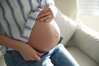 Photo of Pregnant woman touching her belly indoors, closeup