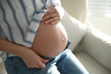 Pregnant woman touching her belly indoors, closeup