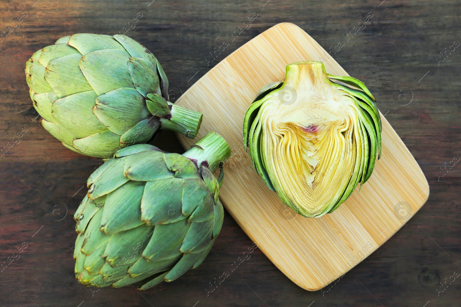 Photo of Whole and cut fresh raw artichokes on wooden table, flat lay