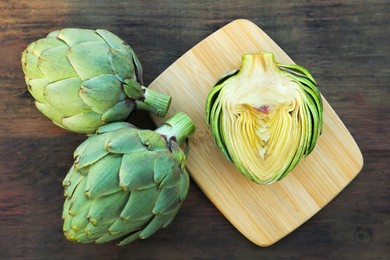 Photo of Whole and cut fresh raw artichokes on wooden table, flat lay