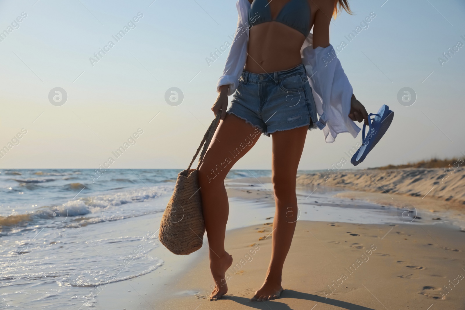 Photo of Woman with beach slippers and bag on sandy seashore, closeup