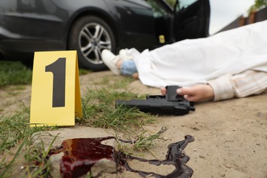 Crime scene markers, dead woman's body and gun outdoors, selective focus