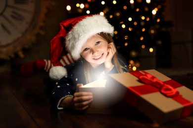 Photo of Cute child opening magic gift box near Christmas tree at night
