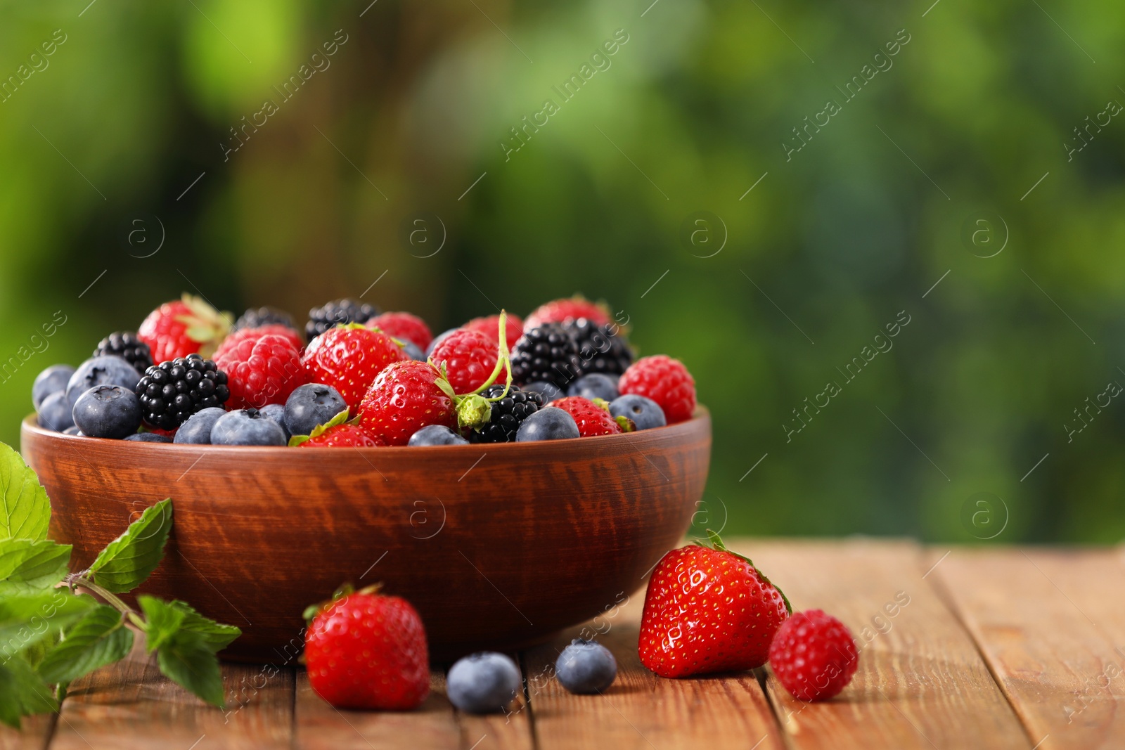 Photo of Bowl with different fresh ripe berries on wooden table outdoors, space for text