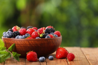 Bowl with different fresh ripe berries on wooden table outdoors, space for text