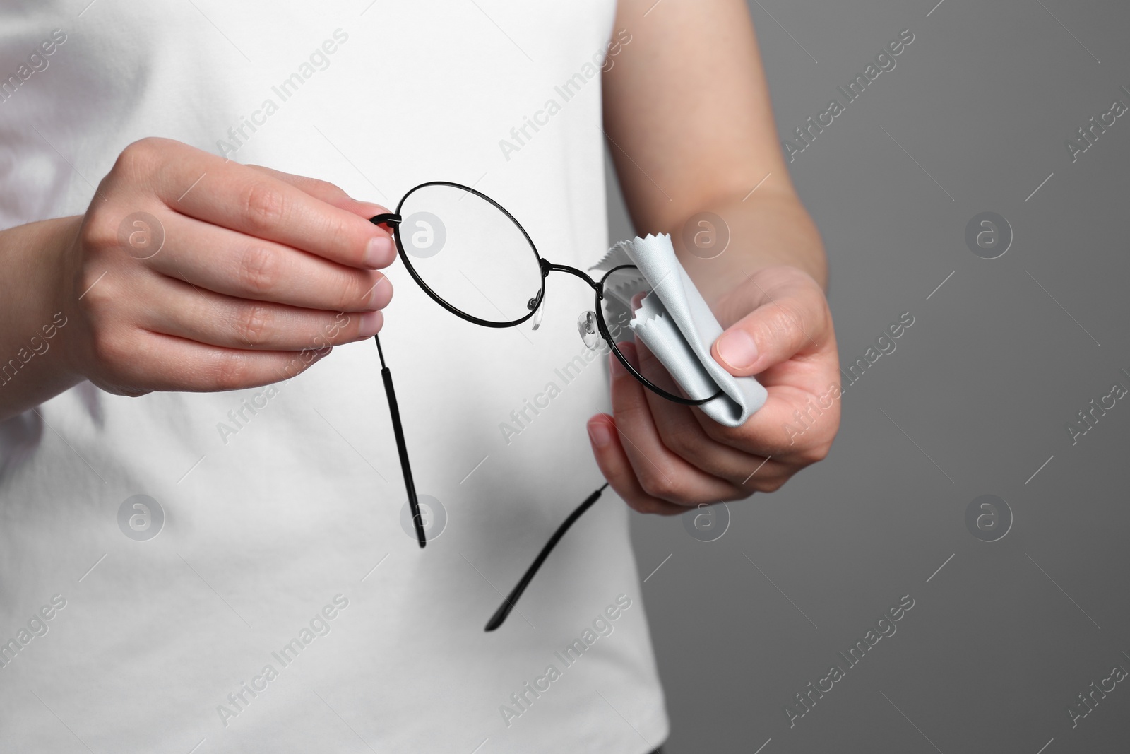 Photo of Woman wiping her glasses with microfiber cloth on grey background, closeup