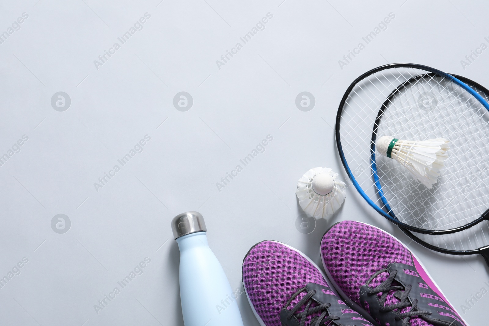 Photo of Feather badminton shuttlecocks, rackets, sneakers and bottle on gray background, flat lay. Space for text