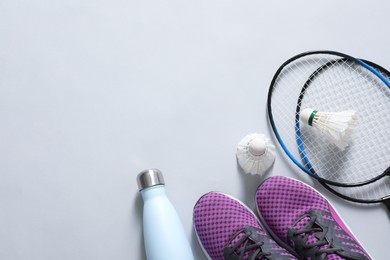Feather badminton shuttlecocks, rackets, sneakers and bottle on gray background, flat lay. Space for text