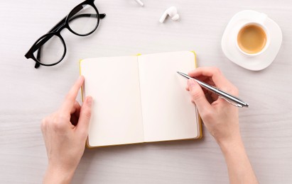 Woman with notebook and pen at white wooden table, top view. Space for text